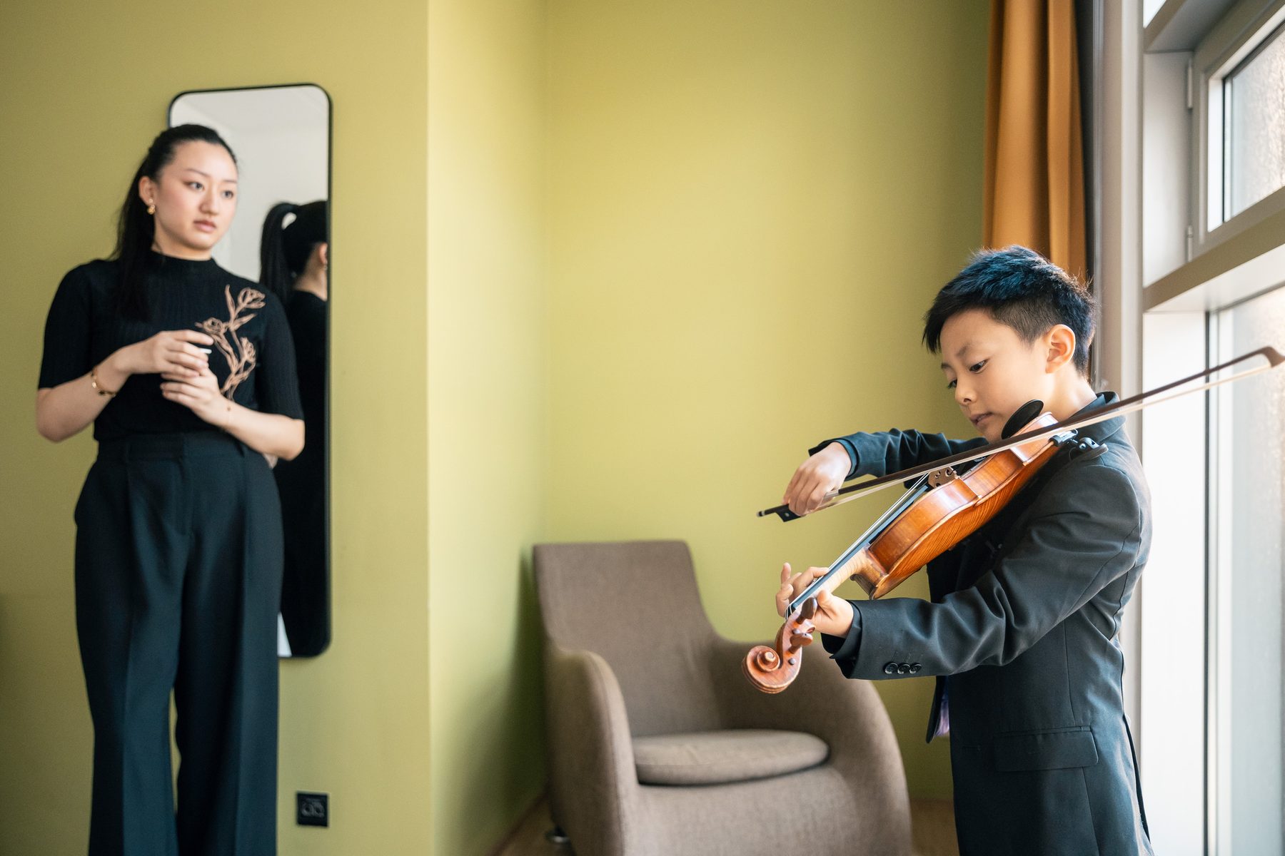 Jonge violist oefent, met zijn docent op de achtergrond